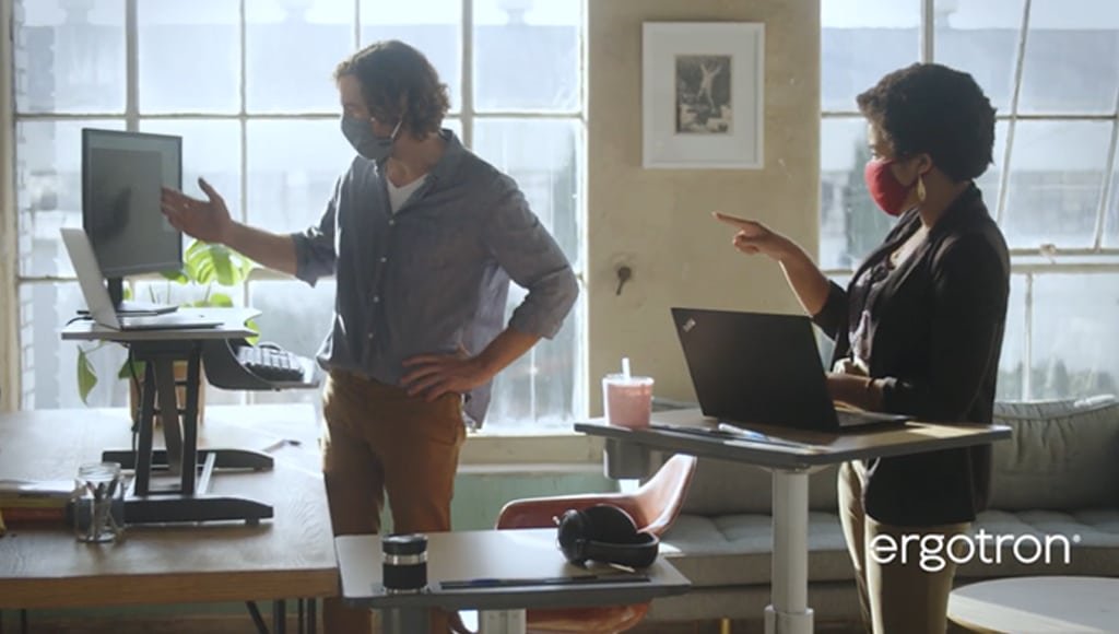 Dua karyawan sedang berkolaborasi saat bekerja menggunakan Ergotron height adjustable desk atau sit stand desk
