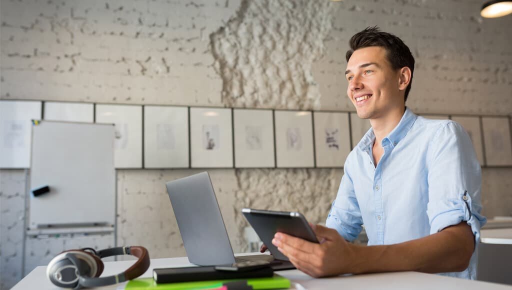 Seorang pegawai kantoran menggunakan laptop dan tablet saat bekerja